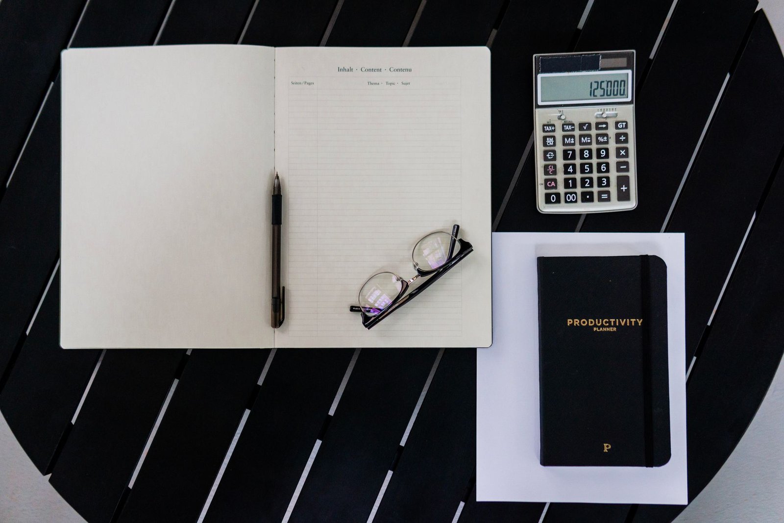 Flat lay of a productivity planner with calculator, pen, and eyeglasses.