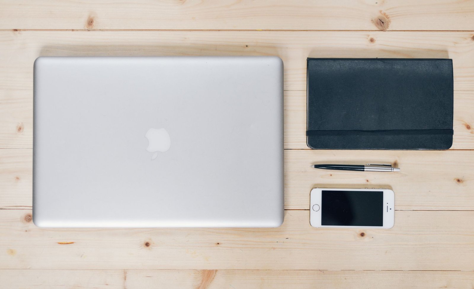 A clean, organized desk featuring a laptop, smartphone, notebook, and pen.