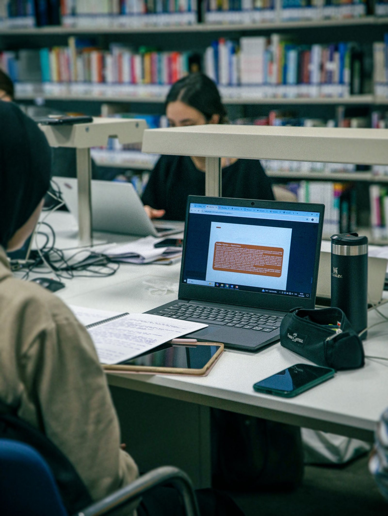 Students studying with laptops and books in a modern library.