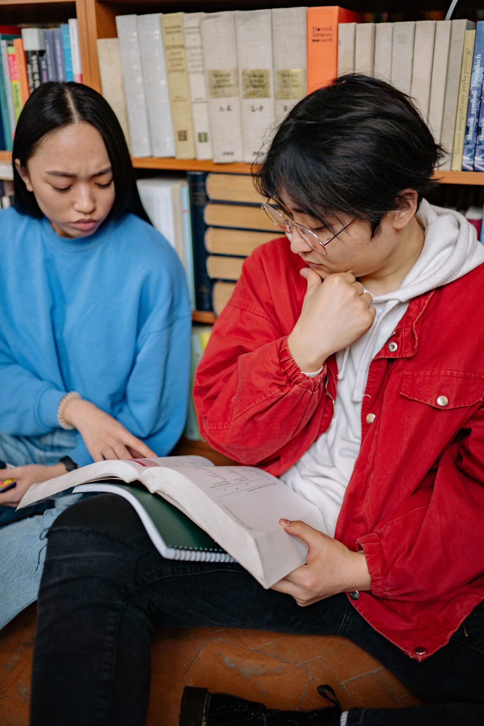 Two students reading and discussing books in a library.