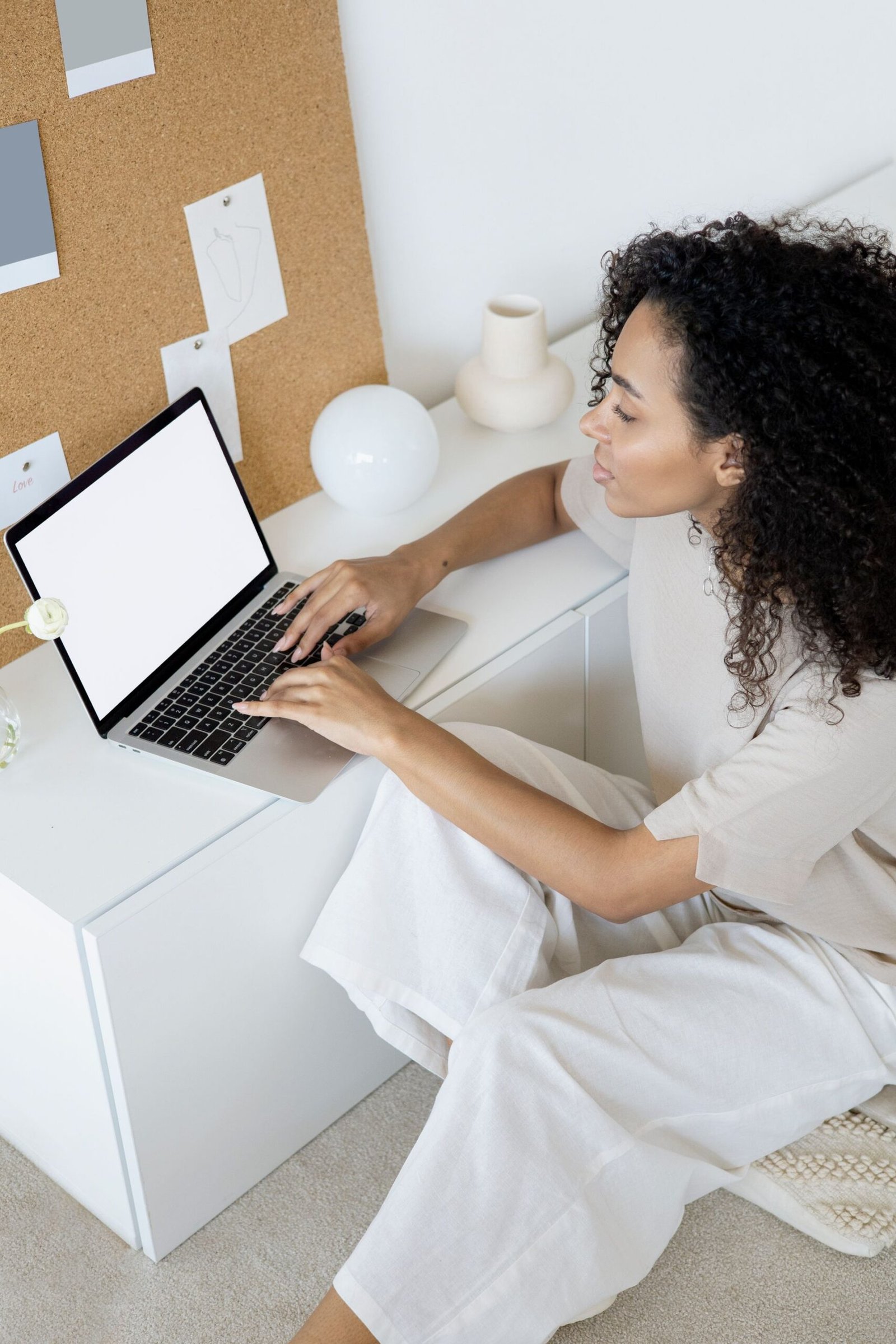 Woman with curly hair typing on a laptop at a home desk.