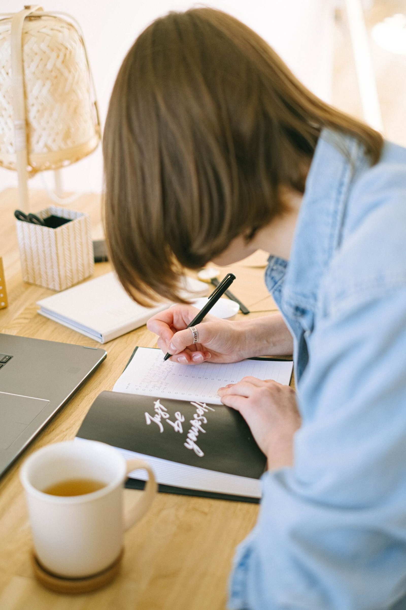 Woman writing notes with a pen in a notebook at her desk.