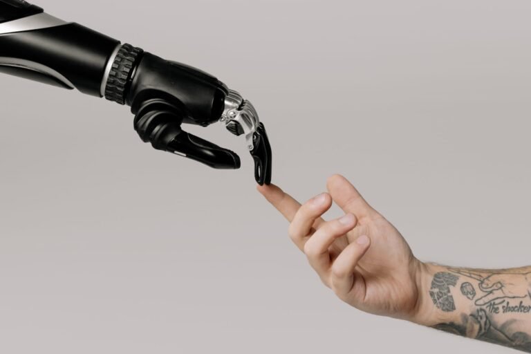 A human hand with tattoos reaching toward a robotic hand on a white background.