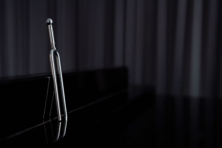 Close-up of a metal tuning fork on a reflective piano surface.