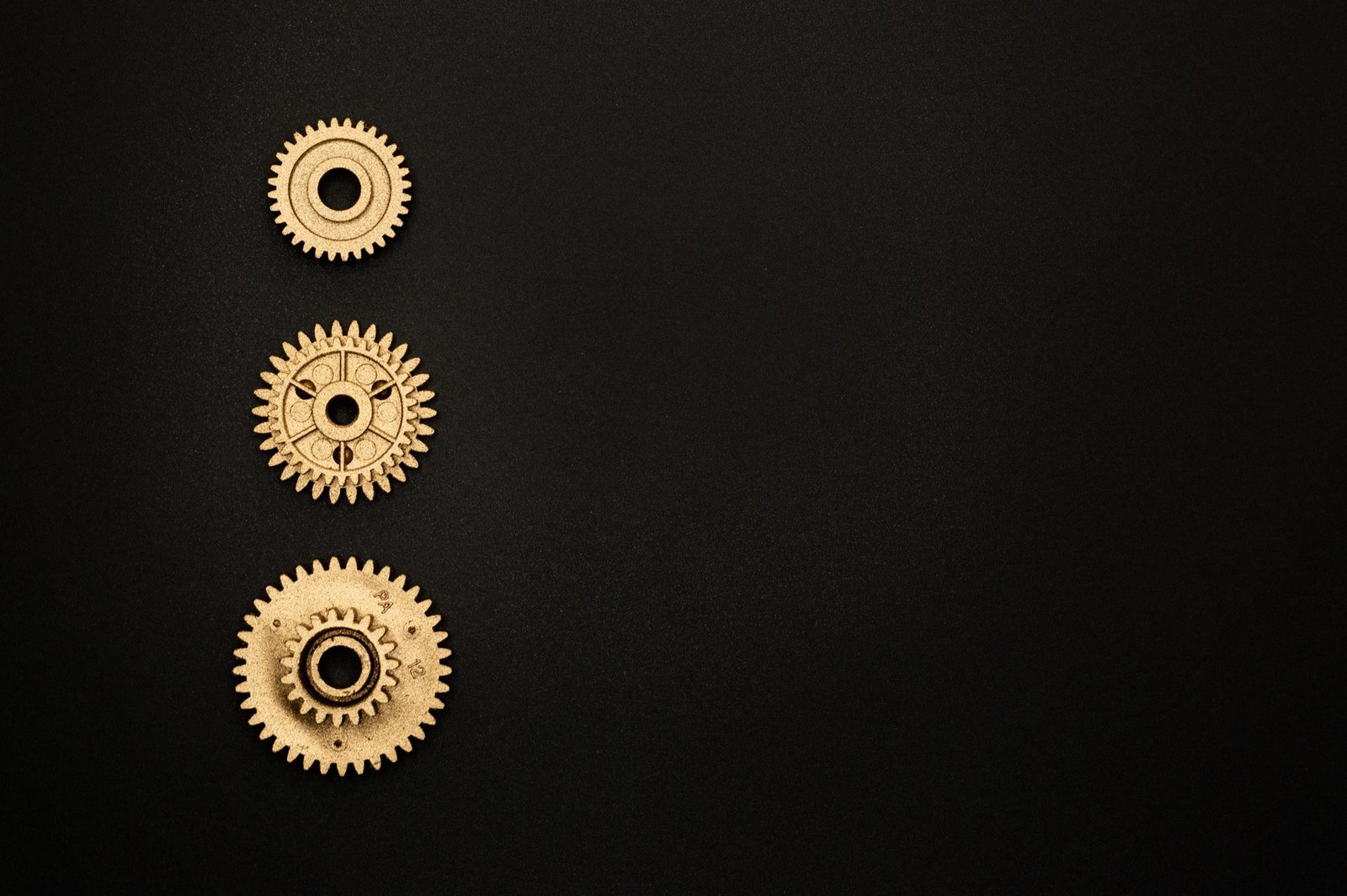 Close-up of three golden gears aligned on a black surface.