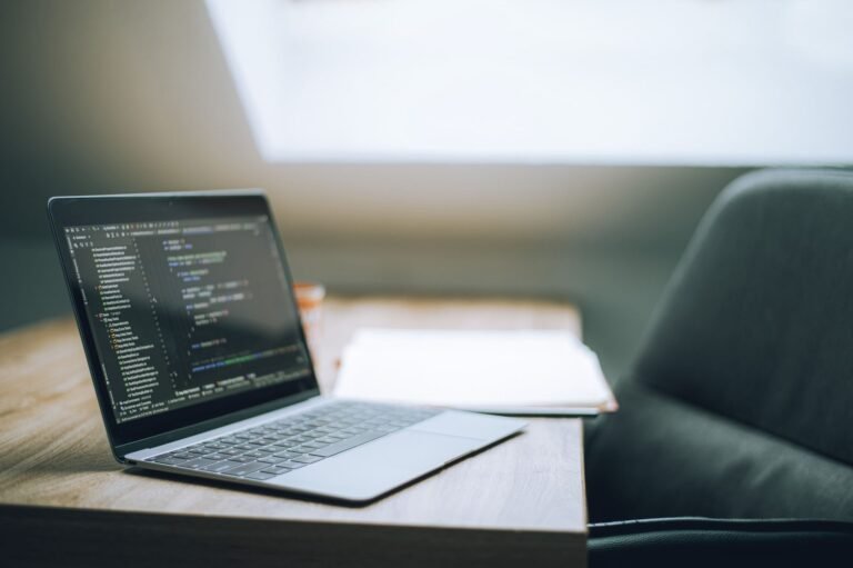 A modern laptop on a desk displaying lines of programming code on its screen.