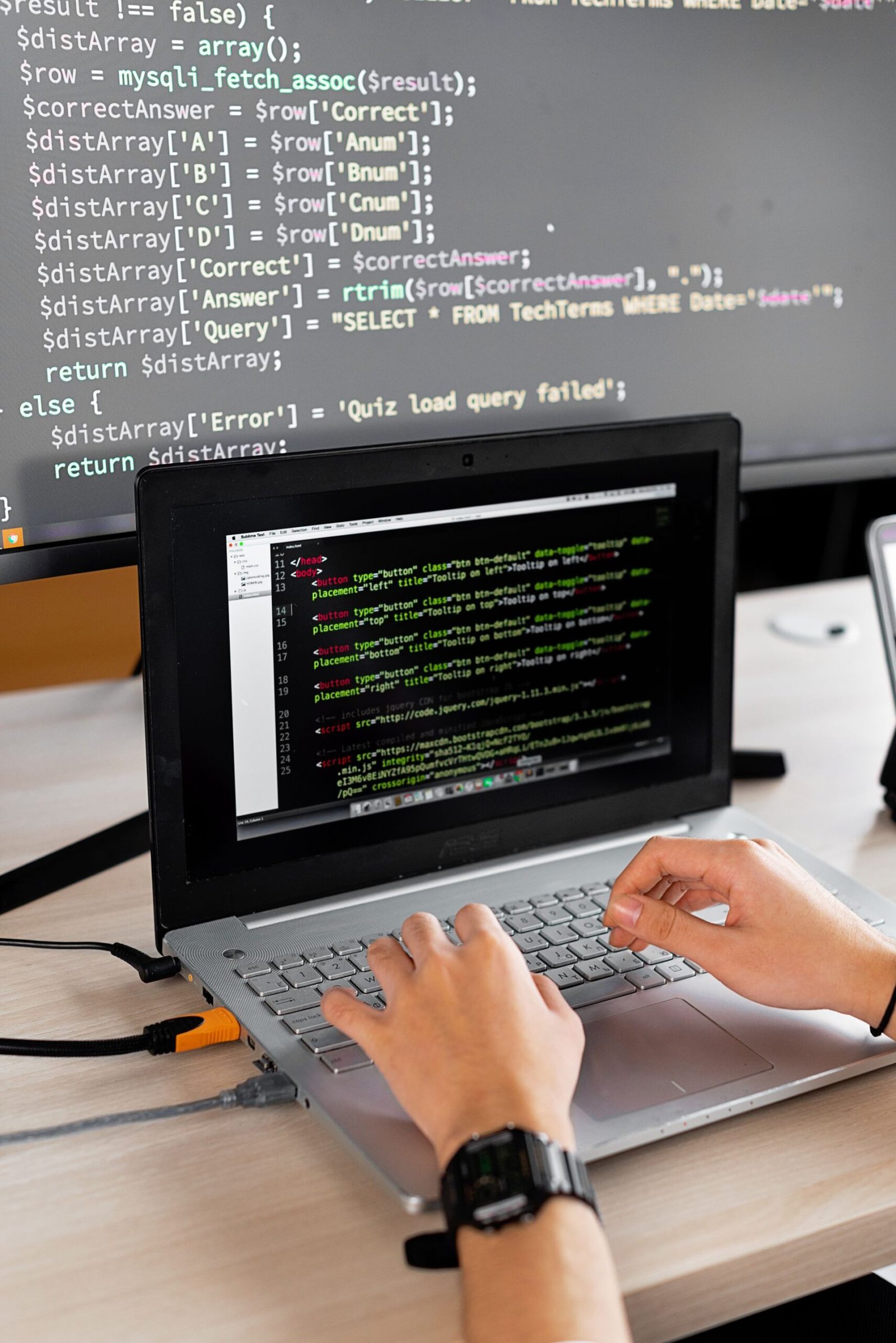 A programmer working at a desk with a laptop and an external monitor.
