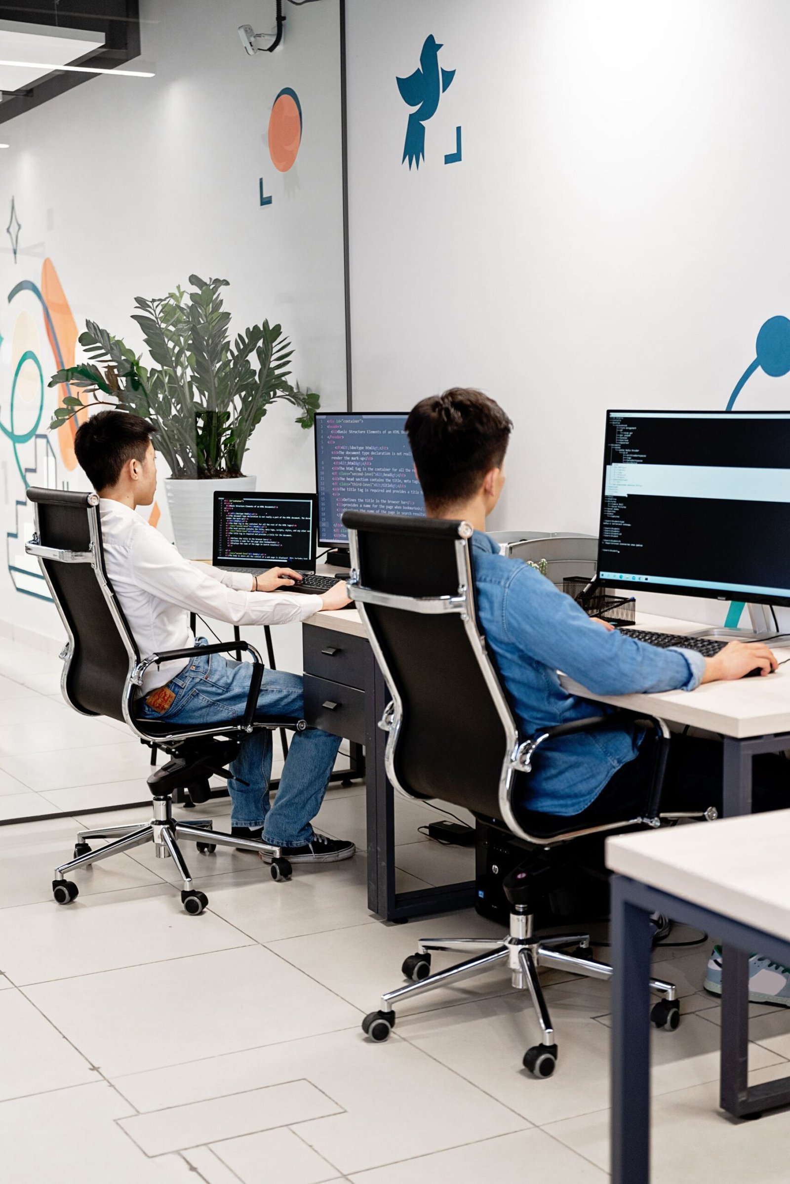 Two programmers collaborating in a bright modern office, coding on monitors.