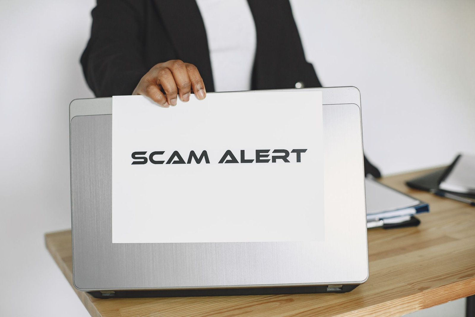 Business person holding a scam alert sign over a laptop.