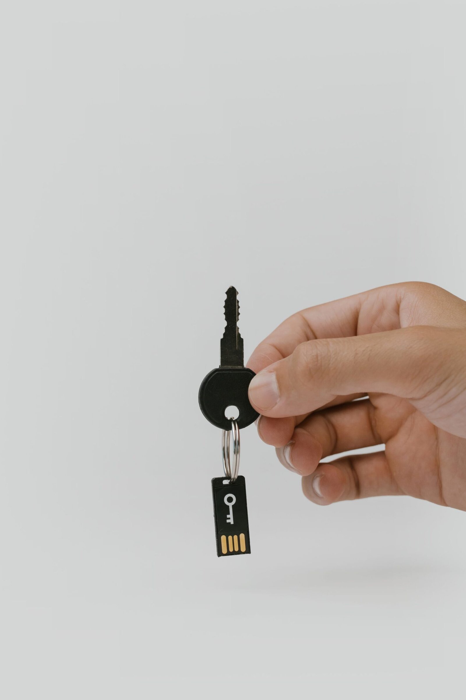 A hand holding a metal key next to a USB flash drive.