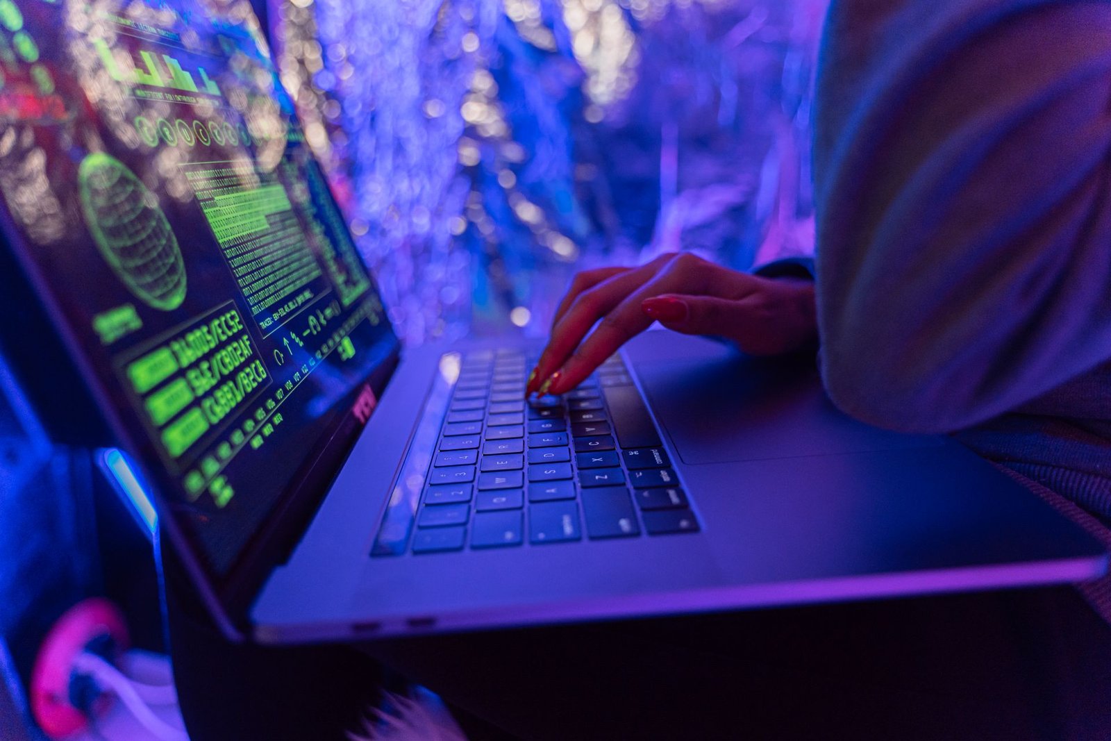Hands typing on a laptop displaying cybersecurity graphics in purple light.