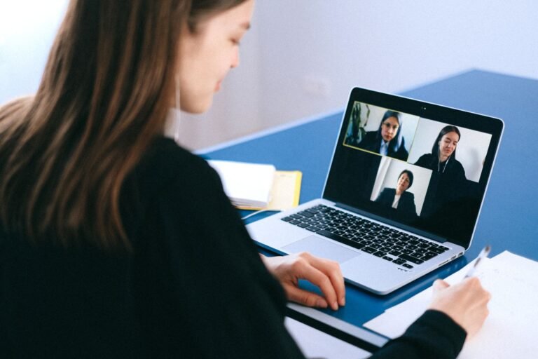 A woman participating in a video conference on a laptop at home while taking notes.