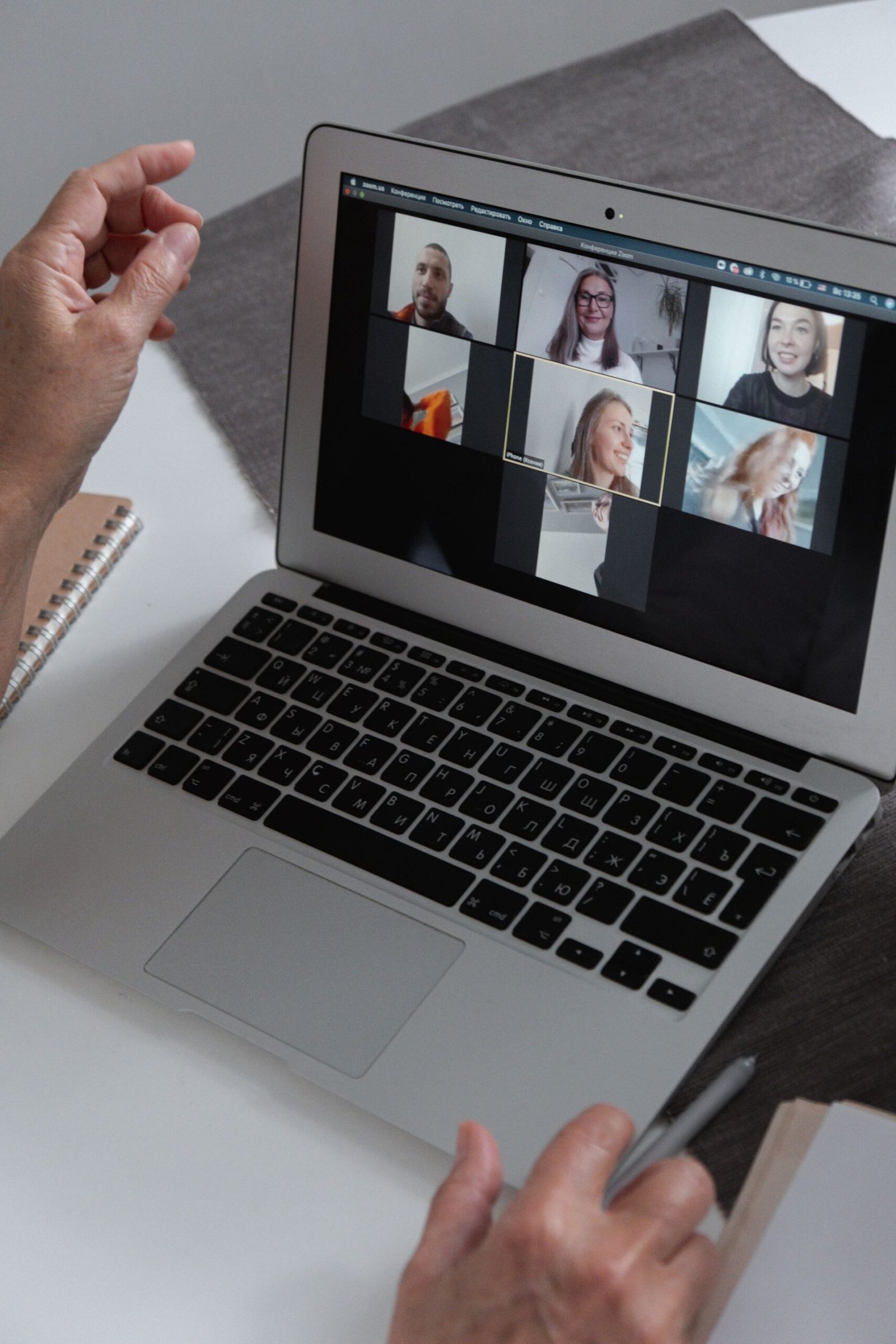 Hands at a laptop showing a group video call in a home office.