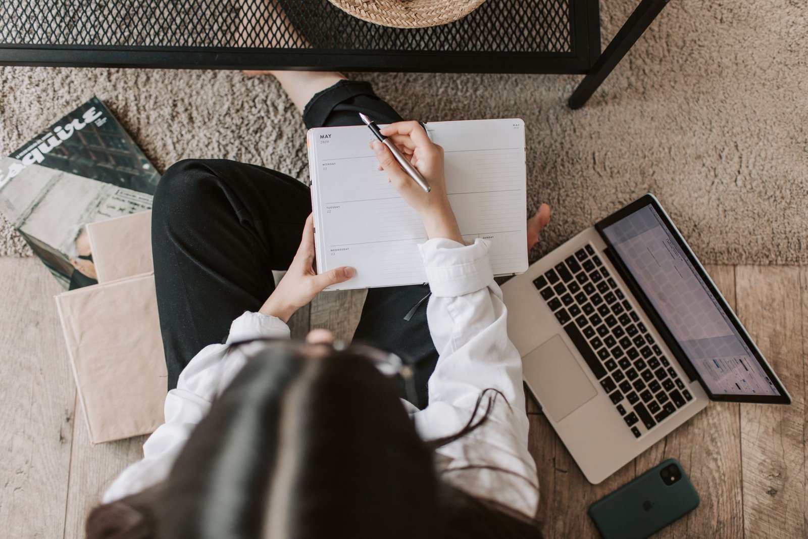 A woman writing in a notebook beside a laptop at home while preparing a job application.