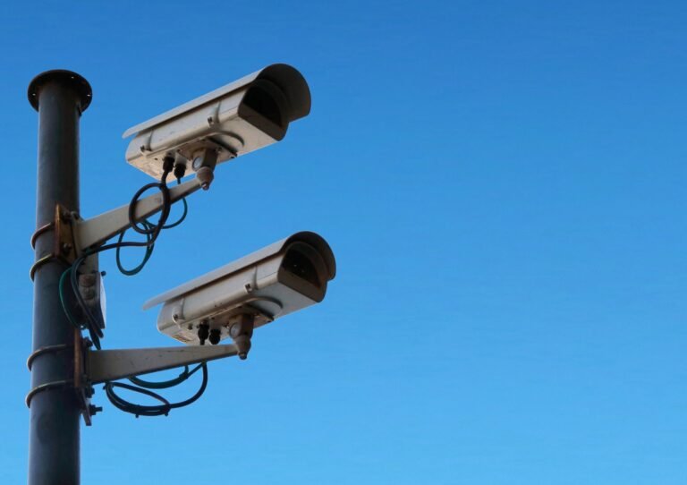 Two white security cameras mounted on a pole against a clear blue sky, representing computer vision surveillance.