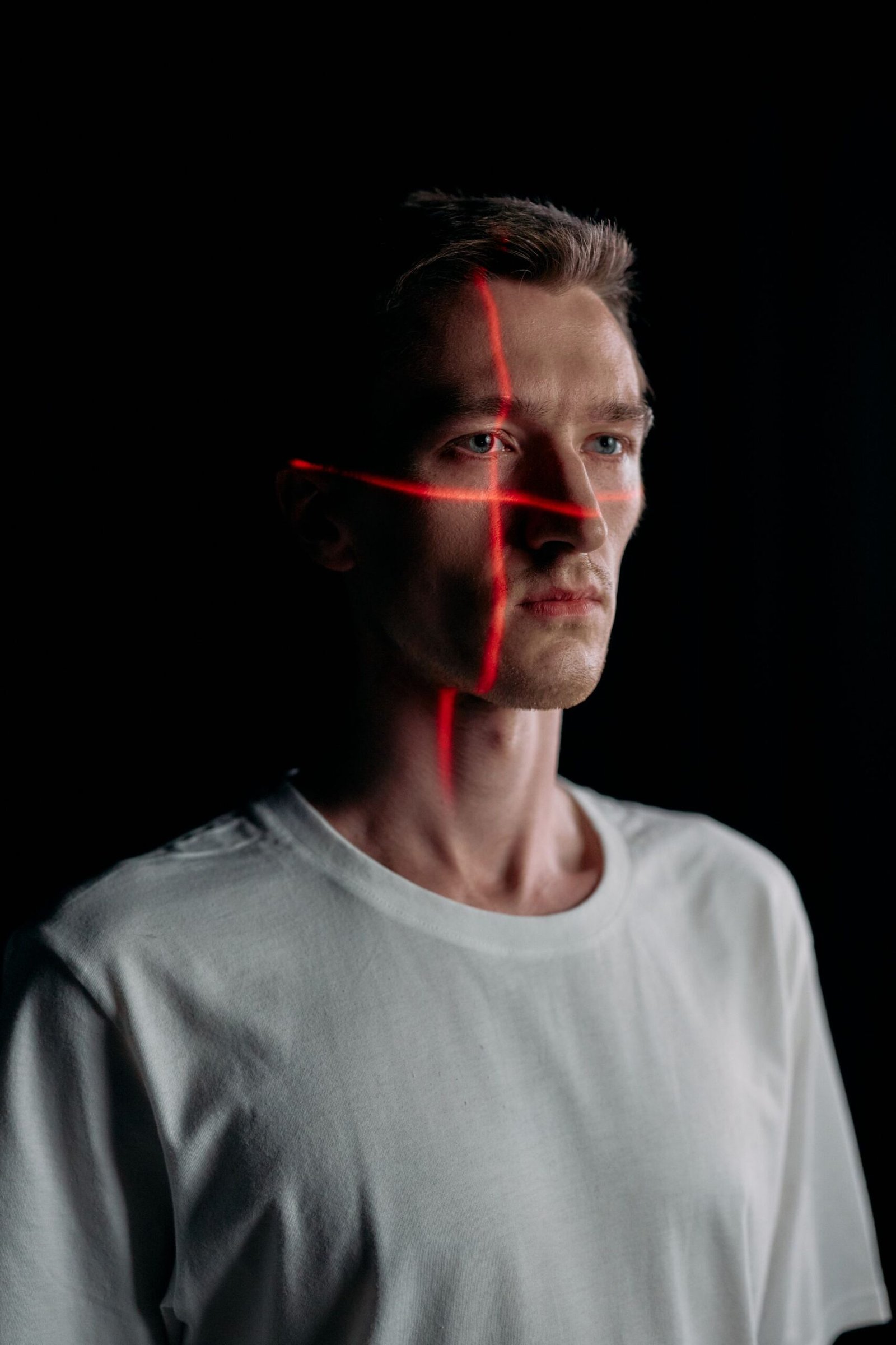 Studio portrait of a man with red laser lines projected across his face, illustrating facial recognition scanning.