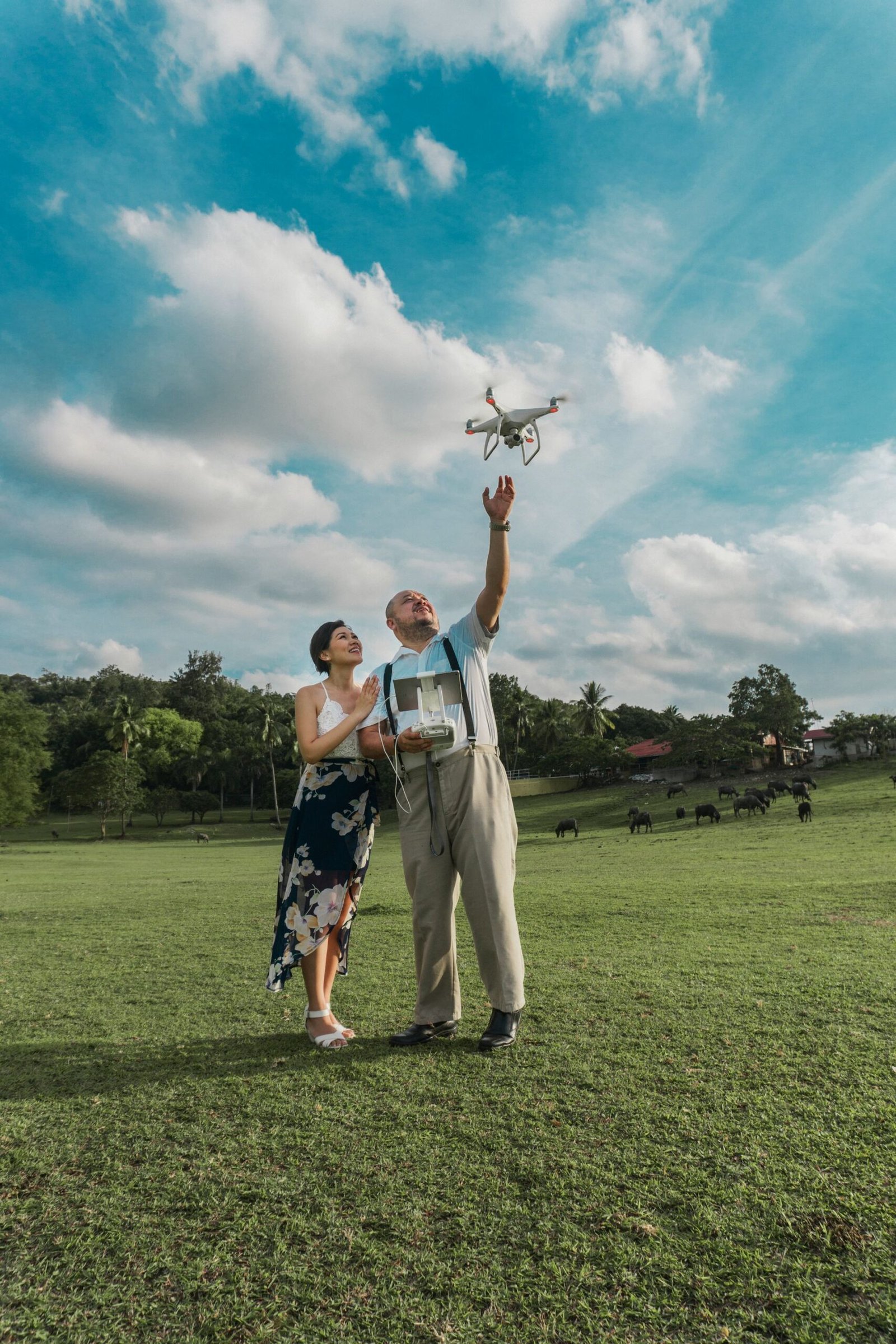 A couple flying a drone together in a sunny park with clear skies and lush greenery.
