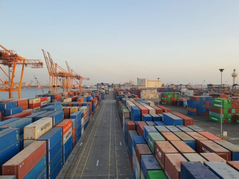 Colorful cargo shipping containers stacked at a harbor at sunrise.