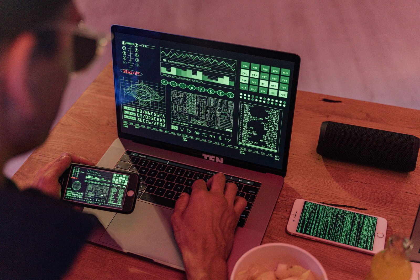 A man working with cybersecurity software on a laptop with a smartphone beside it.