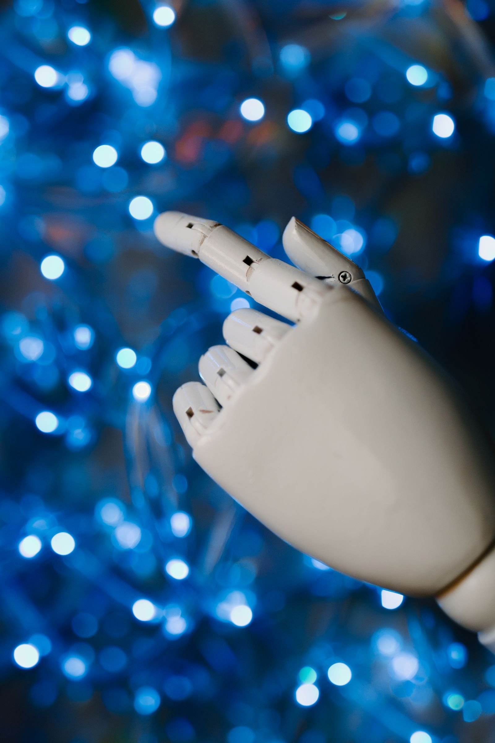 A white robotic hand in close-up against a glowing blue background.