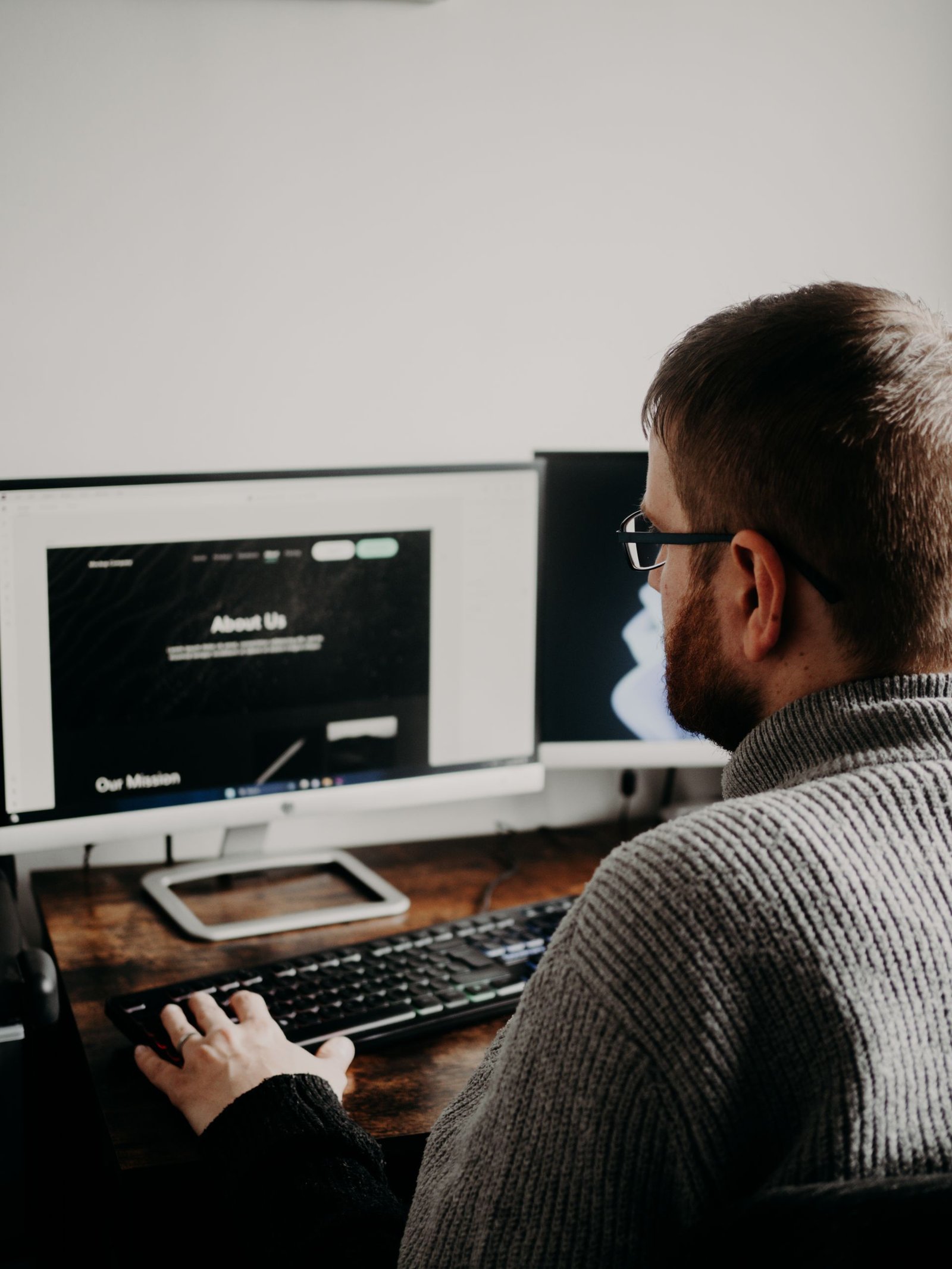 A man working at a home office setup with dual monitors.