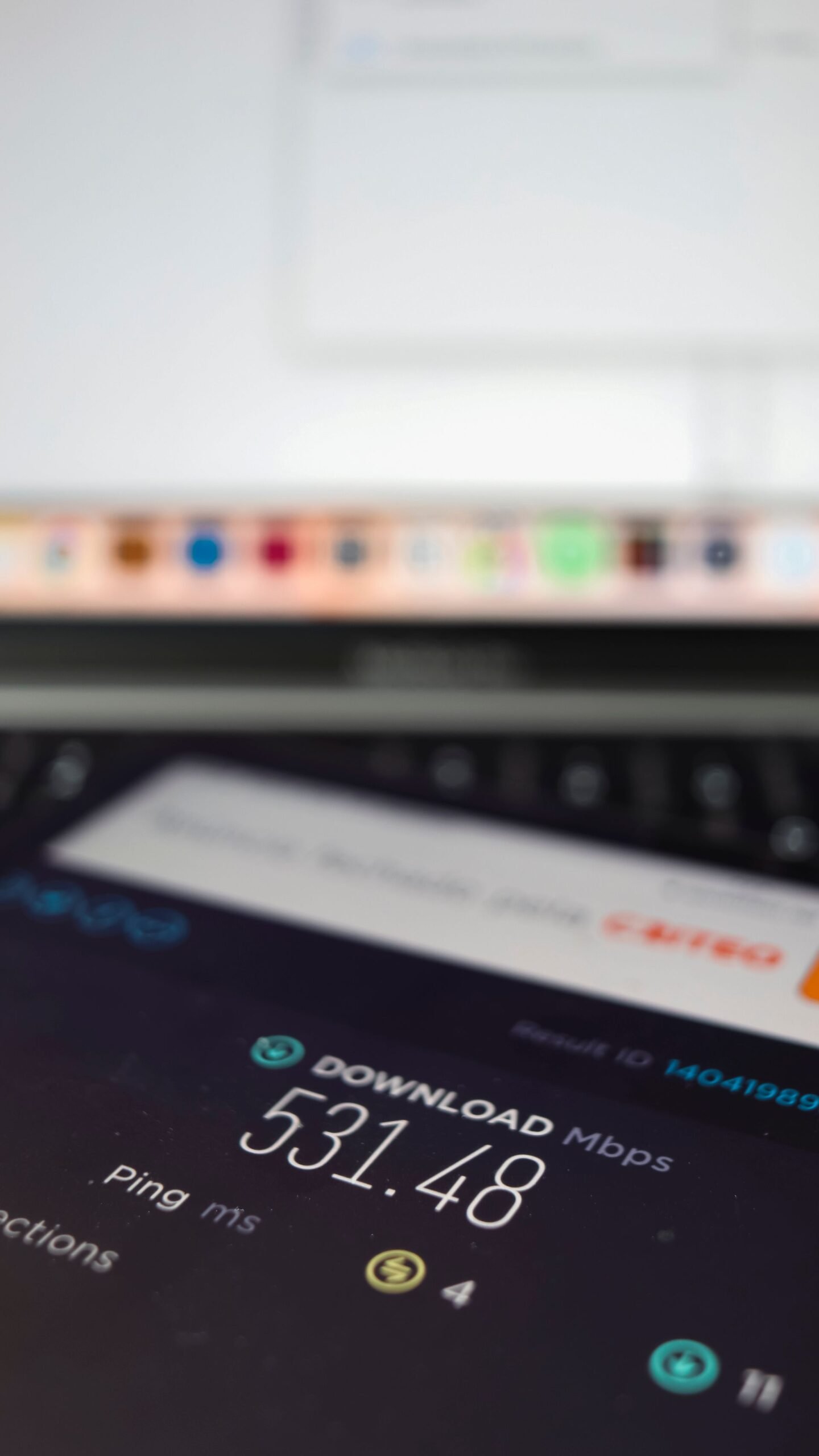 A close-up of a smartphone running an internet speed test with a laptop behind it.
