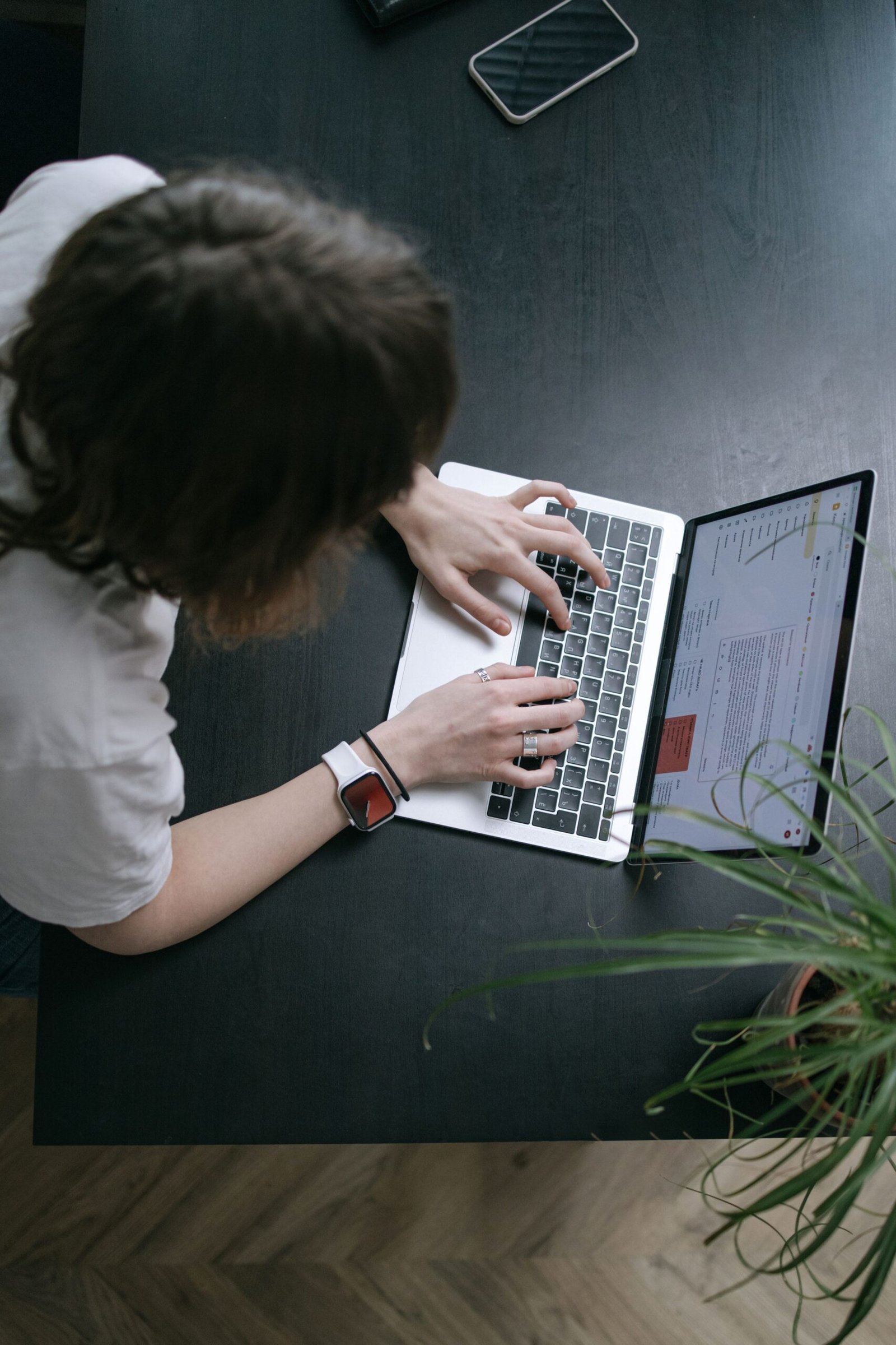 Overhead view of a person typing on a laptop at a tidy desk with a phone and plant.
