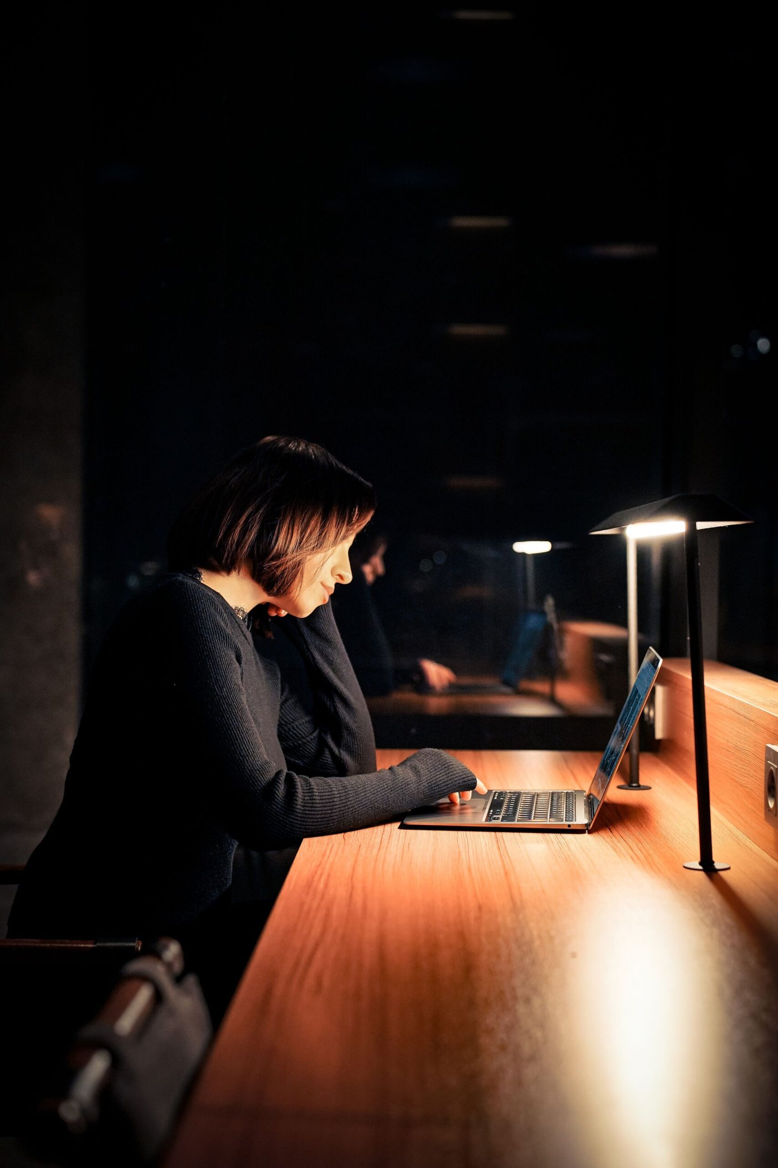 A focused woman working on a laptop late at night in a dimly lit room.