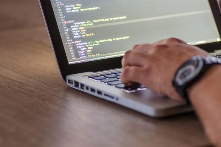 Close-up of a developer's hands typing code on a laptop, with lines of code visible on the screen.