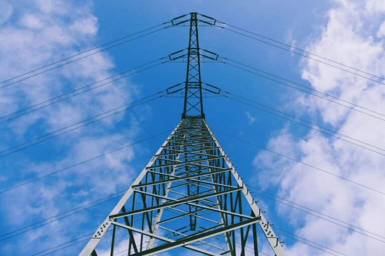 Low-angle view of a tall telecommunications tower against a blue sky with clouds, representing a 5G network cell site.