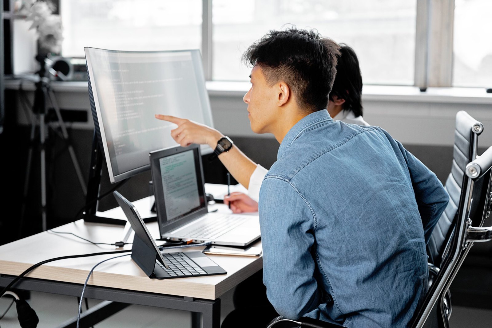Two professionals collaborating at a tech workspace with laptops and monitors.